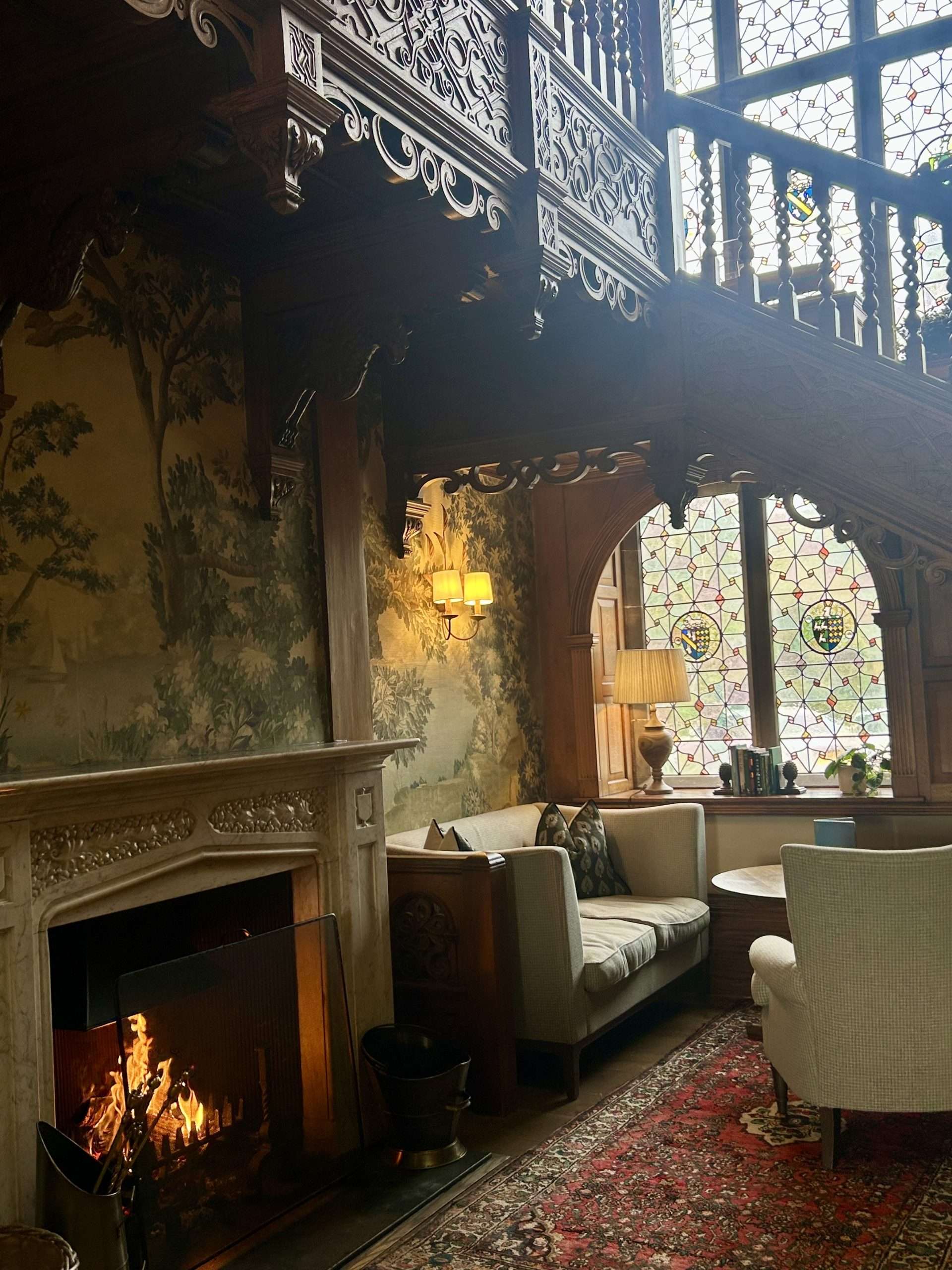 The main foyer wraps guests in warm wooden panelling, ornate cornicing and carved staircases, softened by the steady glow of a crackling fire.