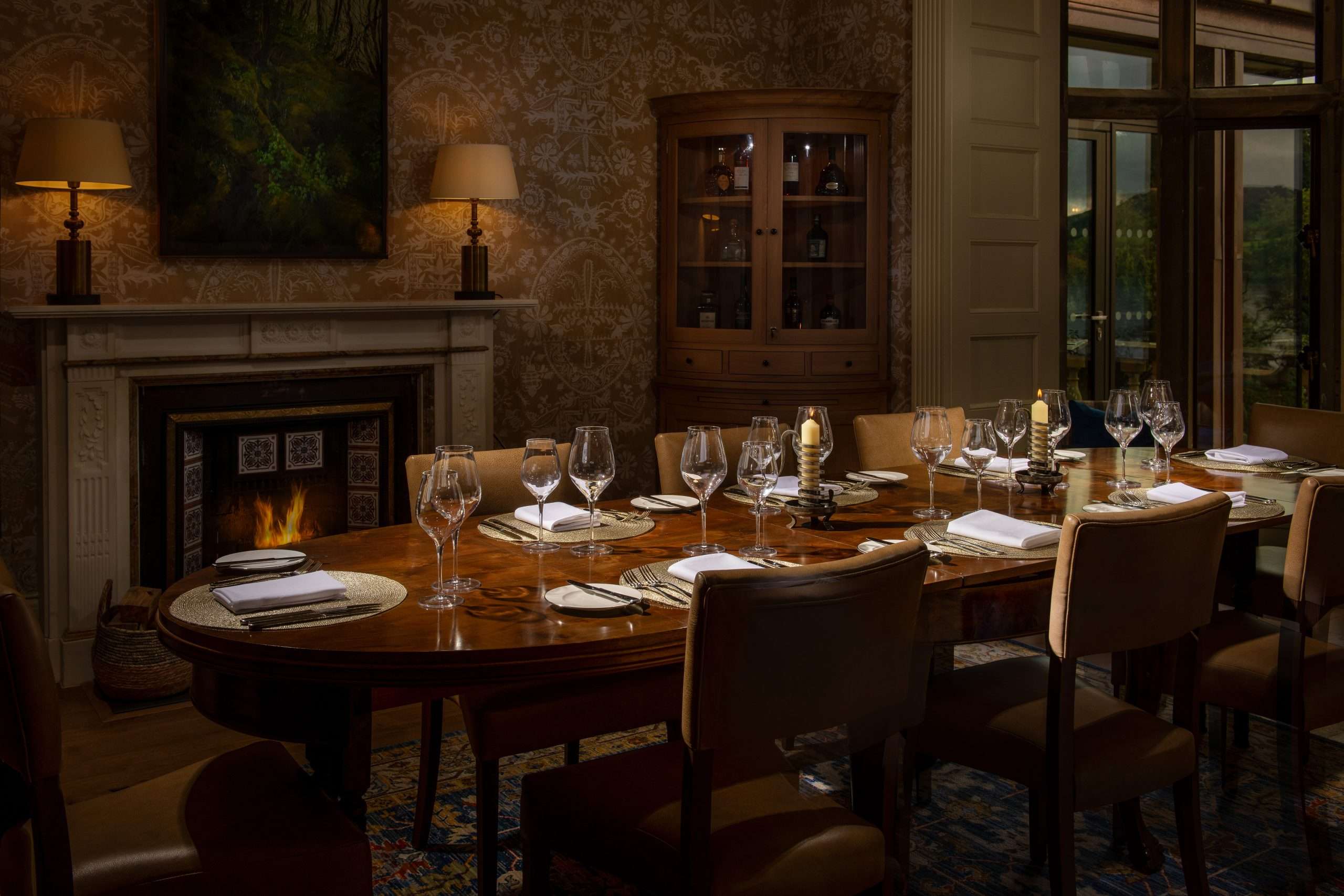 The private dining room at Langdale Chase Hotel. The dark wood table is laid with wine glasses, napkins and pillar candles, in front of an ornate fireplace.